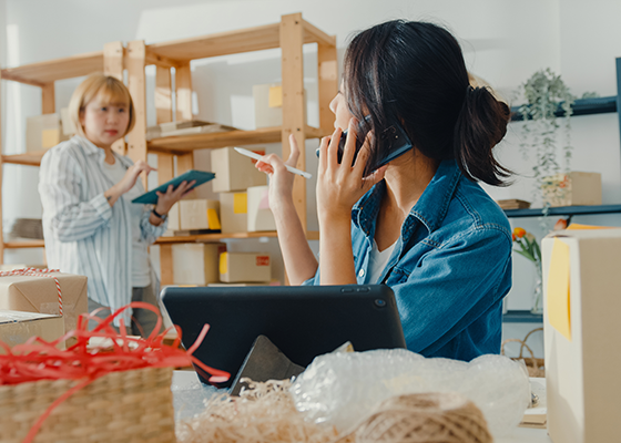 電話中の女性がタブレットで発注と仕入管理をしている従業員に指示を出している様子